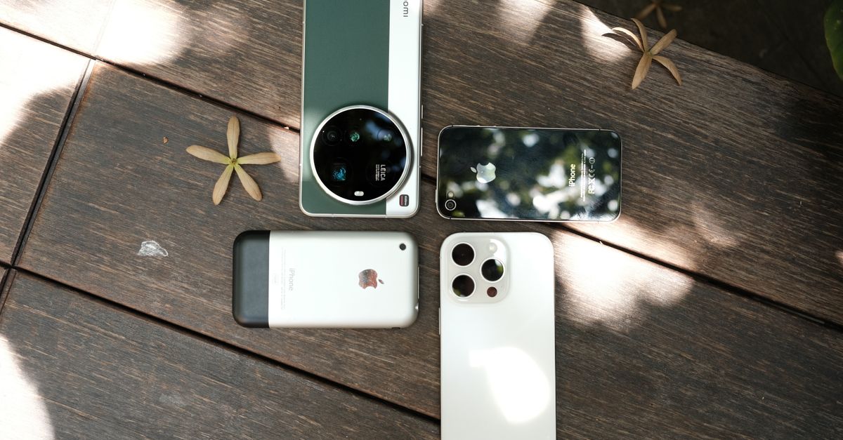 Assorted smartphones displayed outdoors on a wooden table under dappled sunlight.